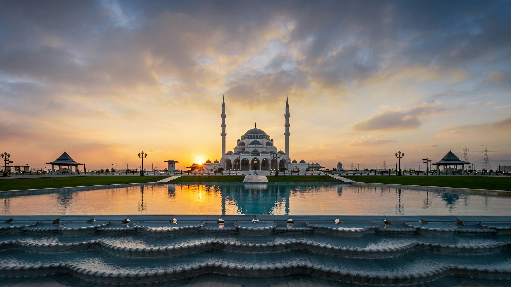 Wondrous Sharjah Mosque reflected in the pool waters on background of the cloudy sunset sky